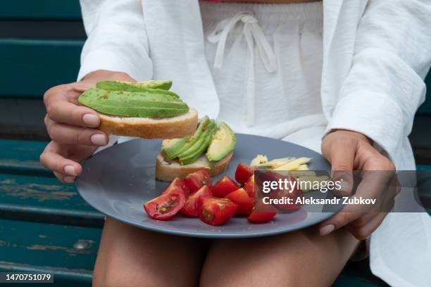 toast or bruschetta of bread and avocado, chopped vegetables and cheese on a plate. a woman is holding a healthy snack in her hands. healthy food, an open sandwich for breakfast or lunch. the concept of vegetarian food. vegan dishes. eating. a simple life - incidental people stock pictures, royalty-free photos & images