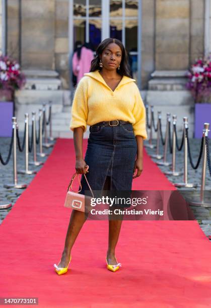 Coco Bassey wears yellow knit with zipper, dark blue denim skirt, rose bag and yellow pointed heels Roger Vivier at Maison de l’Amérique latine on...