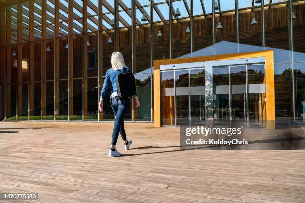 blonde woman walks to the entrance of a glass building - school facade stock pictures, royalty-free photos & images