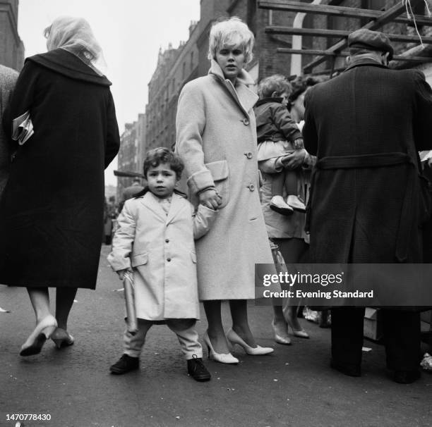 Young boy wearing a Teddy Boy outfit holds his mother's hand at a street market in East London, March 29th 1960.