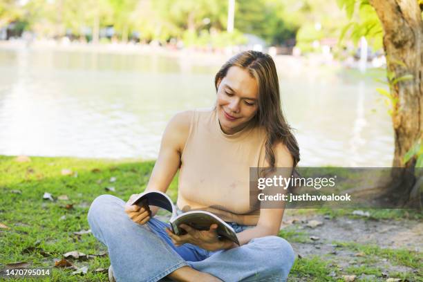 retrato de transgénero tailandés sentado con un libro en un parque público - mujer leyendo libro en el parque fotografías e imágenes de stock