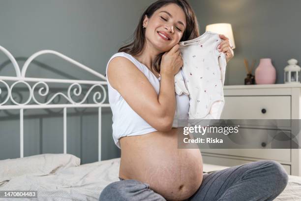 a pregnant woman holding a baby bodysuit - stretch mark stock pictures, royalty-free photos & images