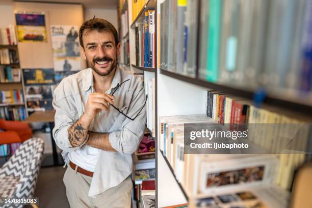 glücklicher student mit brille in der bibliothek stehend, während er in die kamera schaut. - scientific literature stock-fotos und bilder