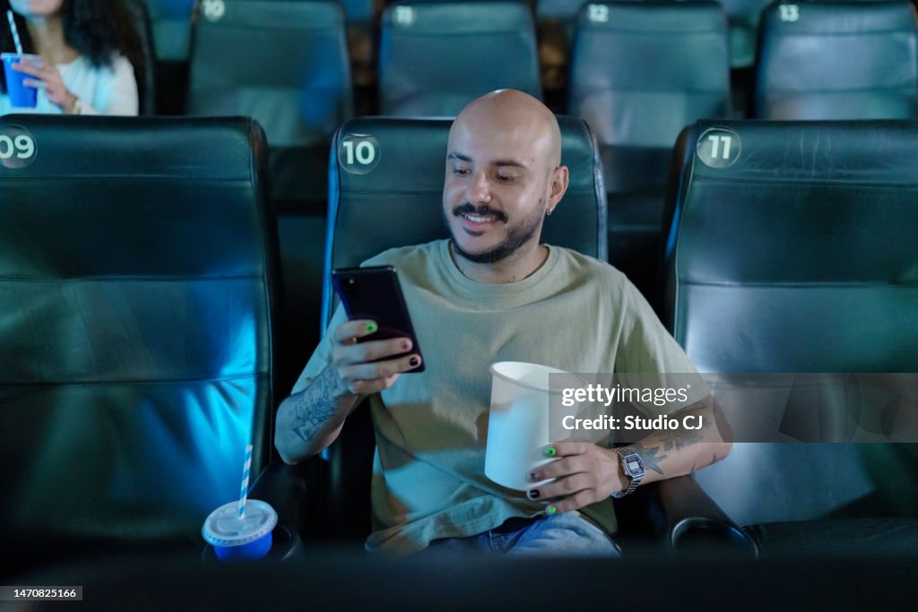 Man alone in movie theater texting on cell phone