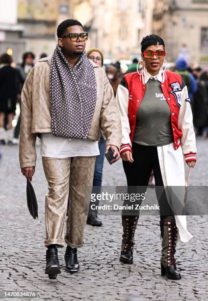 Guest is seen wearing a snakeskin print jacket, snakeskin print pants, black shoes and a black and white scarf with a guest wearing a red and cream...