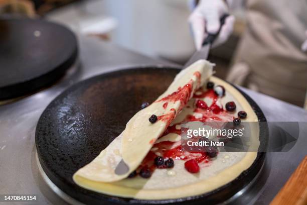 cooking a french crepe, pancake in a pan with mixed berry and cream - crepe textile stockfoto's en -beelden