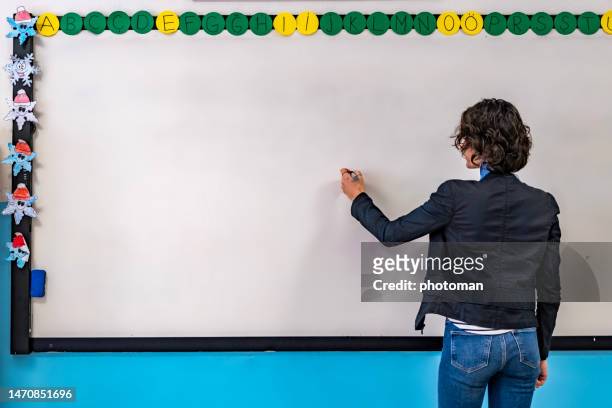 rückansicht einer lehrerin, die auf whiteboard schreibt - interaktives whiteboard stock-fotos und bilder