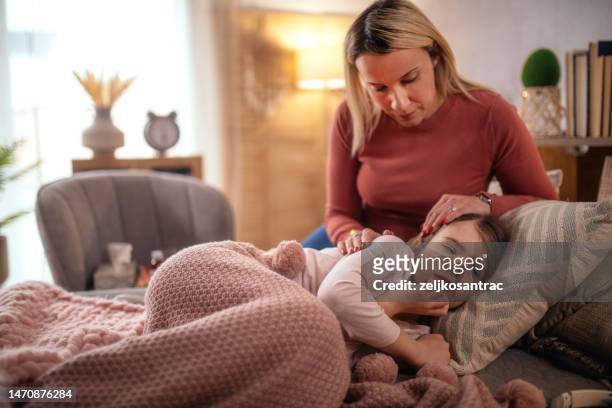 mother checking temperature on sick daughter laying in bed and gives syrup - altitude sickness stock pictures, royalty-free photos & images