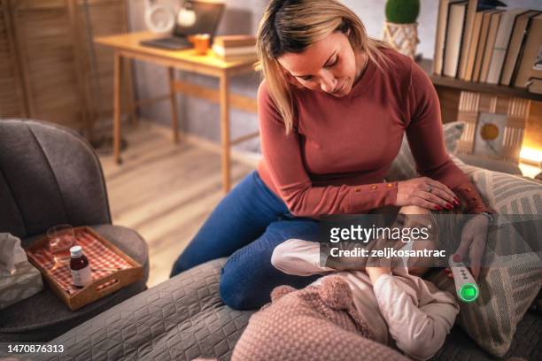 mother checking temperature on sick daughter laying in bed and gives syrup - digital thermometer stock pictures, royalty-free photos & images