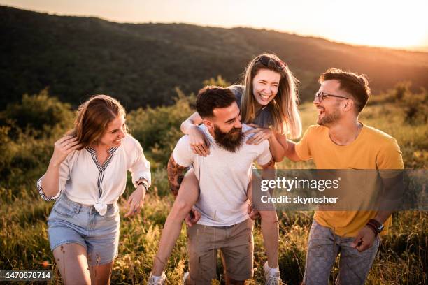 cheerful friends talking while walking up the hill at sunset. - piggy back stock pictures, royalty-free photos & images