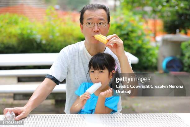 father and child eating ice cream resting after playing at the public park playground. waffle ice cream cone and ice cream bar - filipino family eating fotografías e imágenes de stock