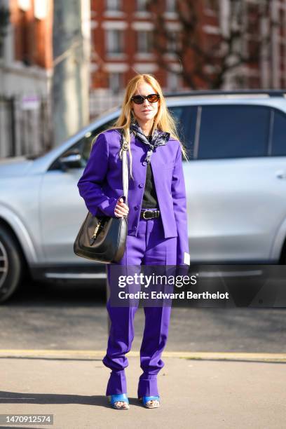 Blanca Miro wears black sunglasses, a black / purple / white print pattern silk scarf, a neon purple buttoned jacket from Off-White, matching neon...