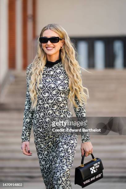 Emili Sindlev wears black sunglasses, gold earrings, a black high neck pullover, a white with black print pattern long sleeves / wrap long tube dress...