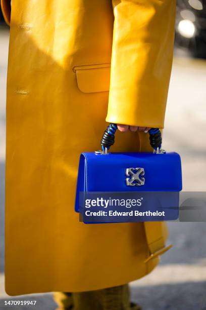 Grece Ghanem wears a yellow mustard shiny leather long coat, khaki tie and dye print pattern denim large cargo pants, a royal blue shiny leather with...
