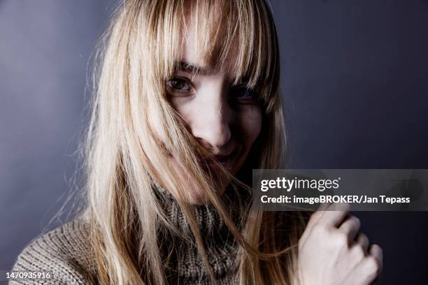 young woman with long blond hair covers one half of her face with a strand of hair and looks saucily into camera, studio shot, cologne, portrait, north rhine-westphalia, germany - pale complexion stock-fotos und bilder