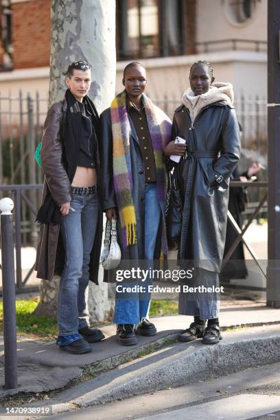 Guest wears silver hair clips, silver and black earrings, a black zipper shirt, a black long scarf, a dark brown shiny leather long coat, a black...