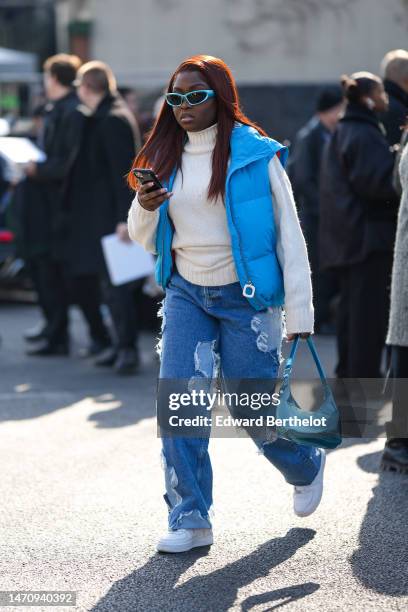 Guest wears pale blue sunglasses, a white wool turtleneck pullover, a flashy blue sleeveless puffer jacket, blue denim with ripped pattern large...