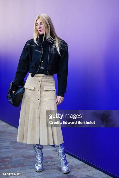 Guest wears gold pendant earrings, a black ribbed wool turtleneck pullover, a black zipper cropped denim jacket, a beige suede pleated / accordion...