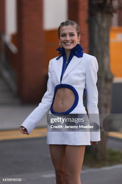 Zoe Pastelle seen wearing silver earrings, a white short blazer jacket dress with a royal blue ribbed ruffled collar / zipper neck and borders and...