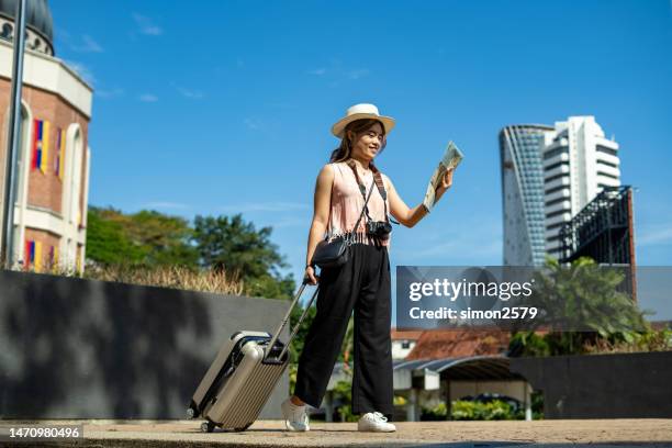 young asian woman walking in city street with her luggage suitcase, active lifestyle and travel concept. - malaysia kuala lumpur merdeka square stock pictures, royalty-free photos & images