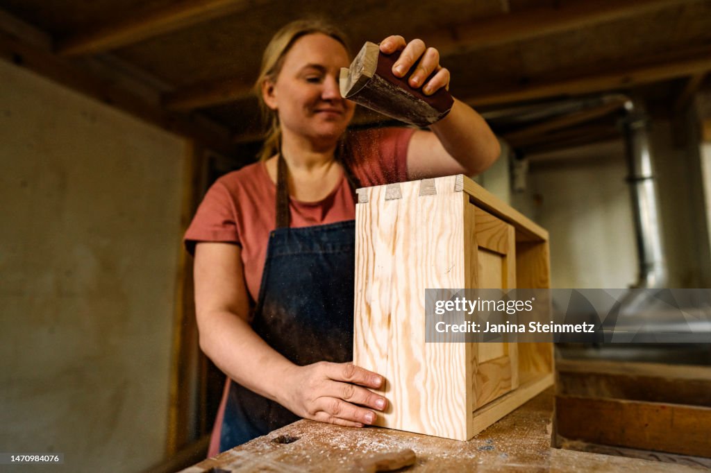 Female entrepreneur sanding hand made wooden drawer