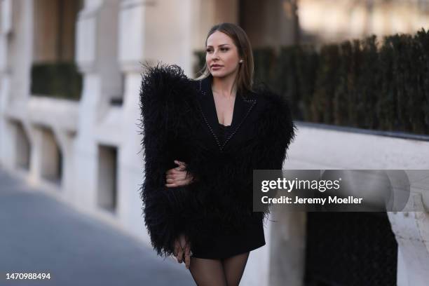 Ginta seen wearing Balmain black jacket with fluffy fur sleeves, Saint Laurent black short skirt, black bandeau top, black tights, during Paris...