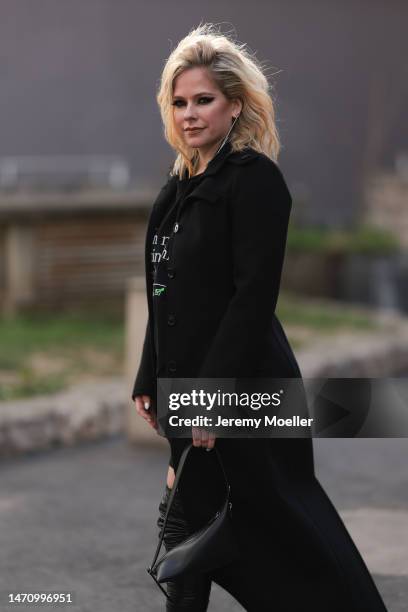Avril Lavigne seen wearing a black long coat, an oversized shirt, a black bag and black high boots before the Courreges show on March 01, 2023 in...