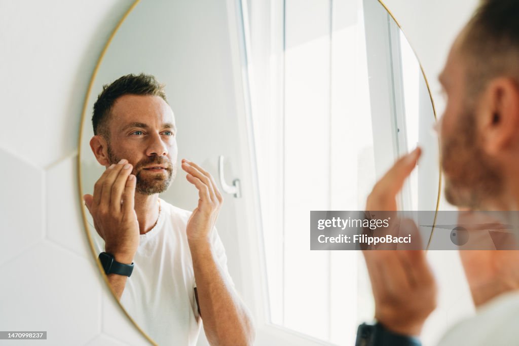 A millennial man is using a face cream in the bathroom