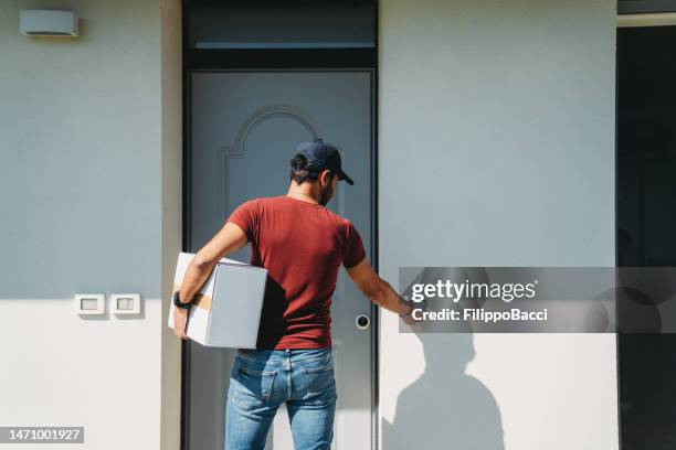 a delivery man is standing in front of the customer's entrance door - deurbel stockfoto's en -beelden