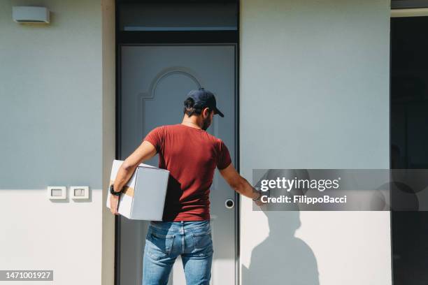 um entregador está parado em frente à porta de entrada do cliente - ringing doorbell - fotografias e filmes do acervo