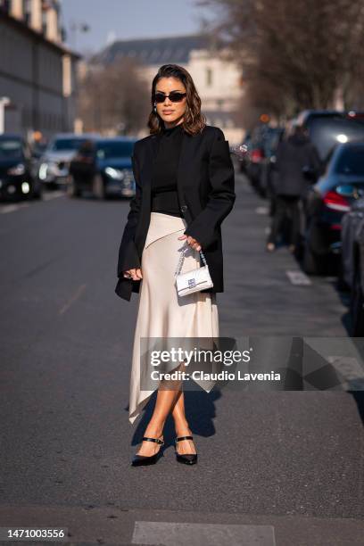 Camila Coelho wears a black turtleneck top, black blazer, cream satin midi skirt, Givenchy bag and heels, outside Givenchy, during Paris Fashion Week...