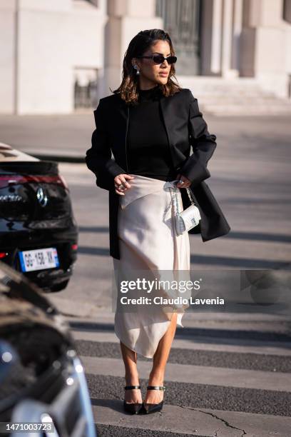 Camila Coelho wears a black turtleneck top, black blazer, cream satin midi skirt, Givenchy bag and heels, outside Givenchy, during Paris Fashion Week...