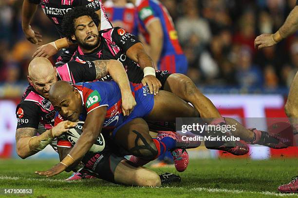 Keith Galloway and Adam Blair of the Tigers tackle Akuila Uate of the Knights during the round 16 NRL match between the Newcastle Knights and the...