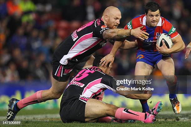 Jarrod Mullen of the Knights tries to break the tackle of Keith Galloway and Ben Murdoch-Masila of the Tigers during the round 16 NRL match between...