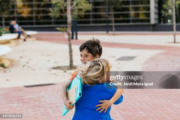 smiling boy holding a folder with school work hugging his mother. - leaving school imagens e fotografias de stock