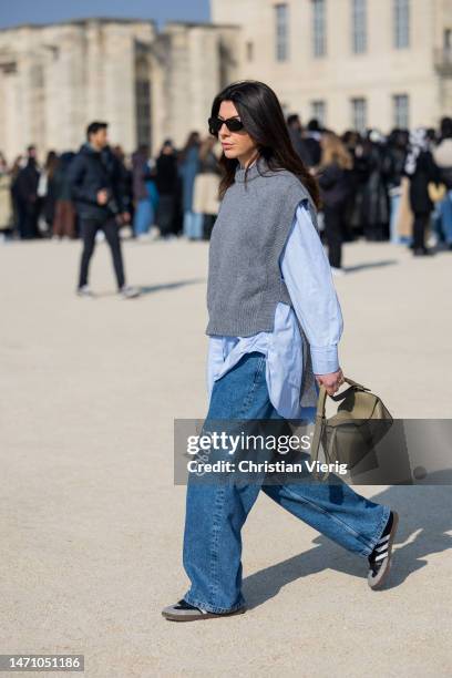 Francesca Saffari wears denim jeans with logo, grey pull under, blue button shirt, green bag outside Loewe during the Paris Fashion Week - Womenswear...