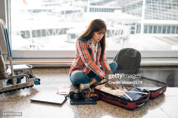 a worried asian woman looking preoccupied inside her suitcase at airport terminal - gestolen-goederen stockfoto's en -beelden