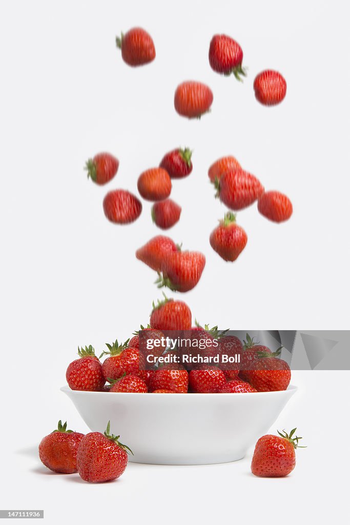 Strawberries falling into a white bowl