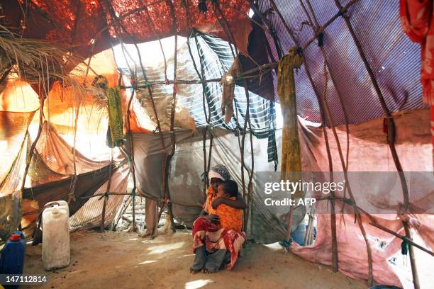 Young girl holds her baby brother in her arms inside a makeshift tent at a camp for Internally Displaced People on the outskirts of Mogadishu on June...