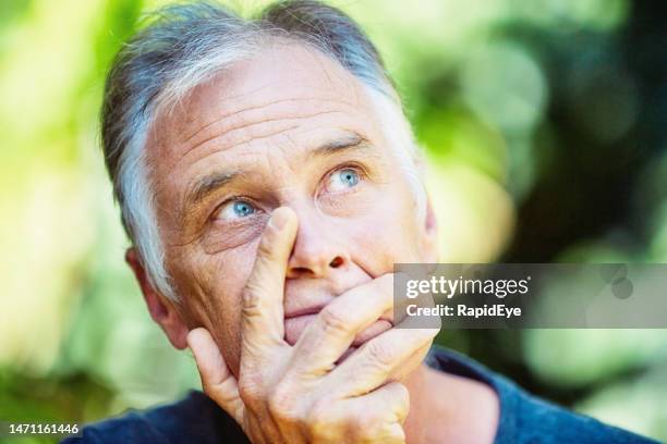 handsome man clutches his face as he stands thinking outdoors in a garden, trying to plan his way ahead - anxiety man stock pictures, royalty-free photos & images