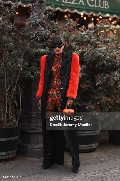 Katya Tolstova seen wearing black Pinko boots, Prada shades, an orange patterned dress by Marcell von Berlin, an orange mini bag, a black long coat...