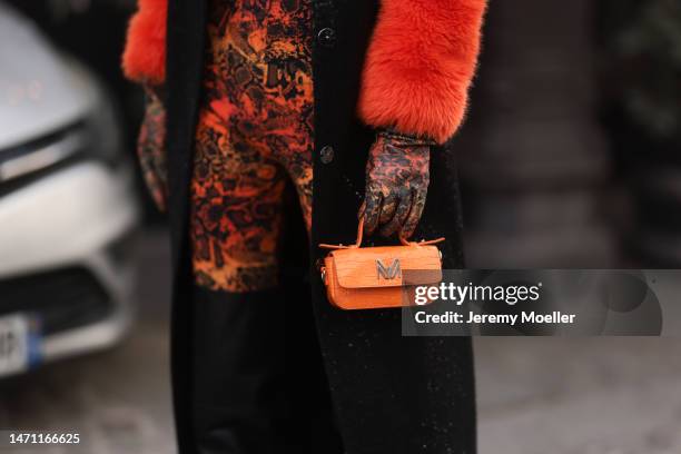 Katya Tolstova seen wearing black Pinko boots, Prada shades, an orange patterned dress by Marcell von Berlin, an orange mini bag, a black long coat...