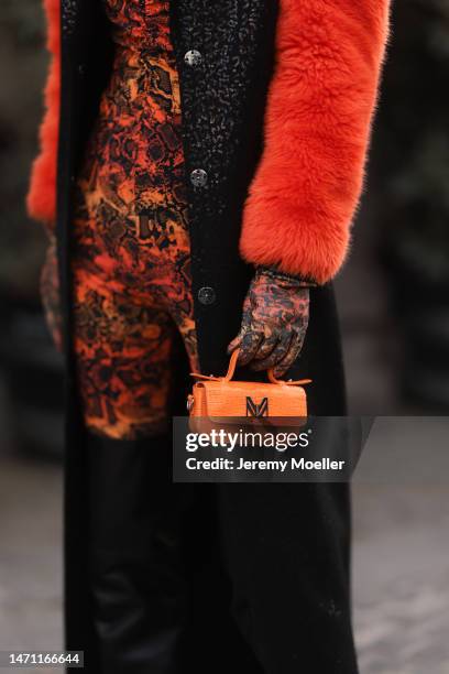 Katya Tolstova seen wearing black Pinko boots, Prada shades, an orange patterned dress by Marcell von Berlin, an orange mini bag, a black long coat...