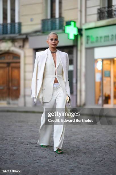 Caroline Daur wears gold and silver large chain necklaces from Tiffany, a white belted long blazer gilet, a white buttoned blazer jacket, white high...