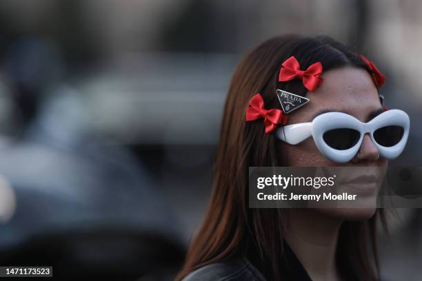 Amelie Stanescu wears a prada hairclip, red ribbon hairclips, white inflated loewe sunglasses, black leather bomber jacket and a white t-shirt,...