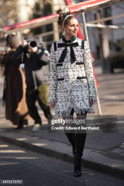 Olivia Palermo wears a black tulle knot hair clip, a pink velvet headband, diamonds and white pearls pendant earrings, a white with black embroidered...