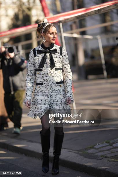 Olivia Palermo wears a black tulle knot hair clip, a pink velvet headband, diamonds and white pearls pendant earrings, a white with black embroidered...