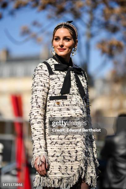 Olivia Palermo wears a black tulle knot hair clip, a pink velvet headband, diamonds and white pearls pendant earrings, a white with black embroidered...