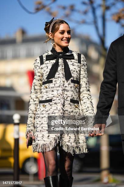 Olivia Palermo wears a black tulle knot hair clip, a pink velvet headband, diamonds and white pearls pendant earrings, a white with black embroidered...