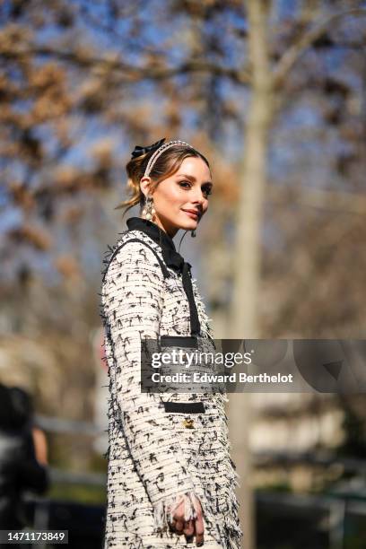 Olivia Palermo wears a black tulle knot hair clip, a pink velvet headband, diamonds and white pearls pendant earrings, a white with black embroidered...